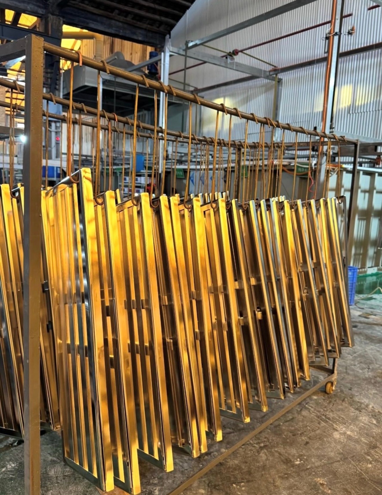 Plated steel components with a gold finish hanging on a rack in a Chinese finishing facility after the plating process